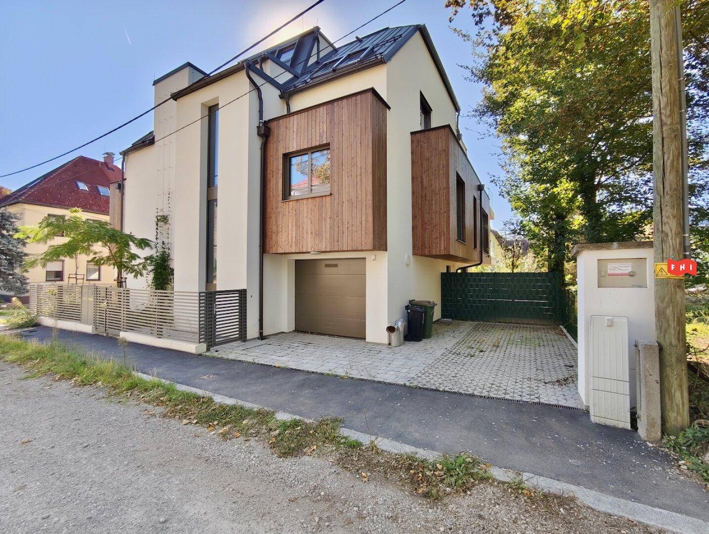 Modernes Gebäude mit weißer Fassade und Holzverkleidung, Garage und gepflasterter Einfahrt.