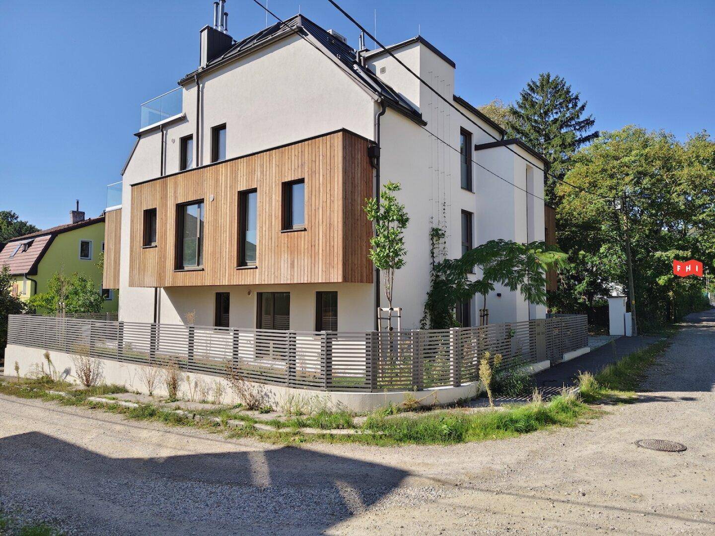Seitenansicht des modernen Gebäudes mit Holzverkleidung und großen Fenstern, eingebettet in Grün.