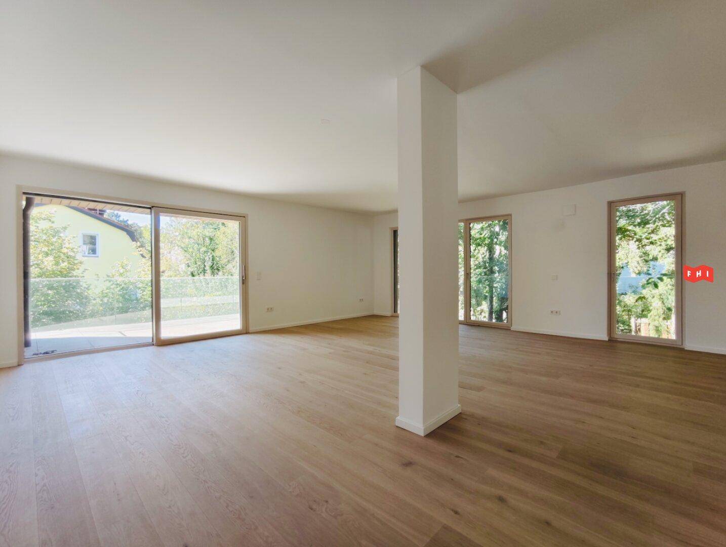Lichtdurchfluteter Wohnbereich mit Zugang zu einem Balkon und Blick ins Grüne.