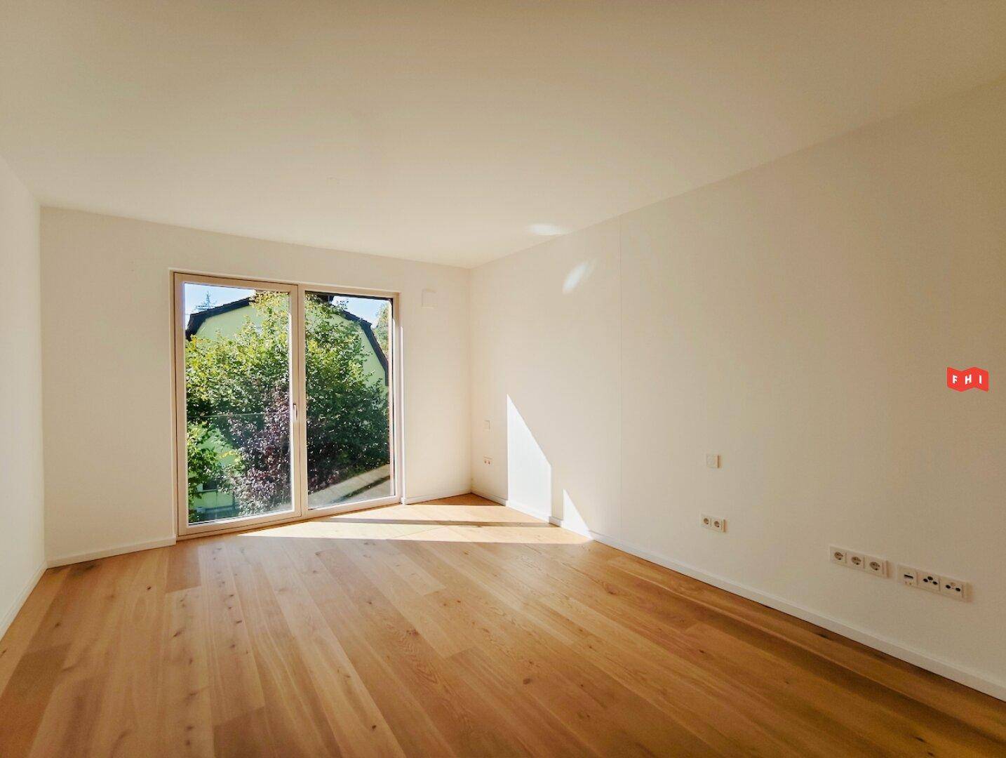 Helles Schlafzimmer mit Eichenparkett und großem Fenster, das viel Sonnenlicht hereinlässt.