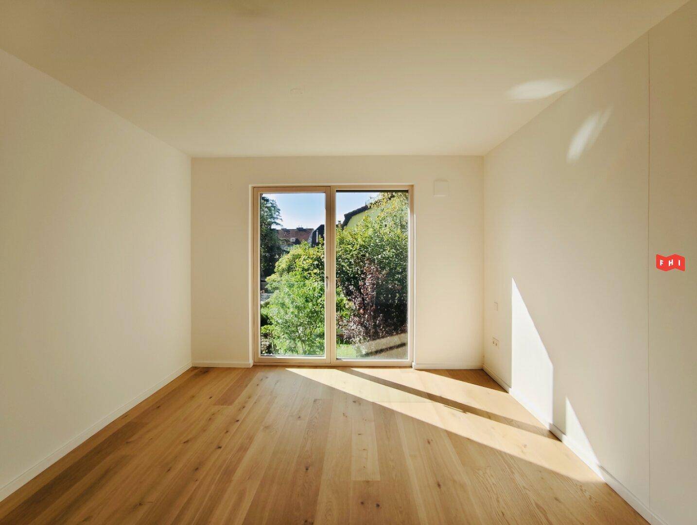 Geräumiges Zimmer mit Parkettboden und Fenster, das einen Blick ins Grüne bietet.