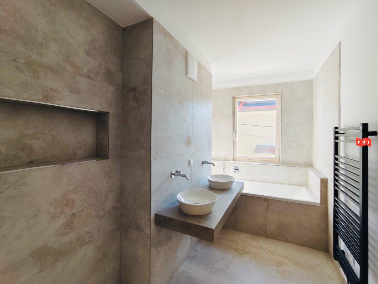 Modernes Badezimmer mit Doppelwaschbecken, Badewanne und beigefarbenen Fliesen.