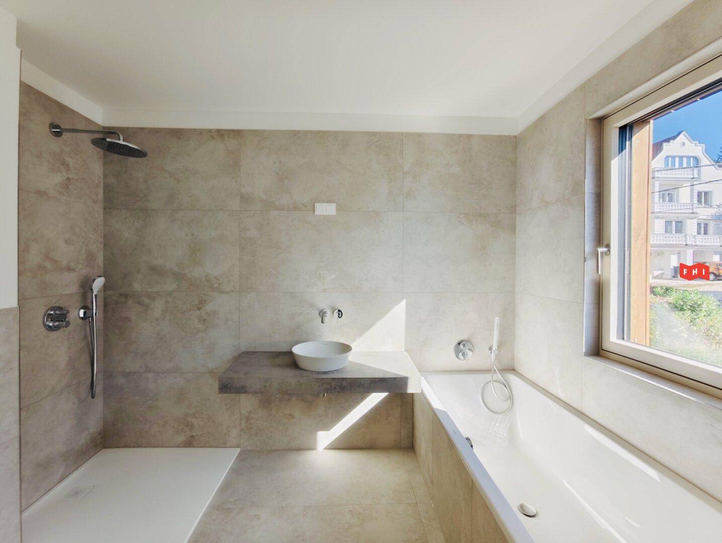 Modernes Badezimmer mit Badewanne, Dusche und Fenster, ausgestattet mit beigefarbenen Fliesen.