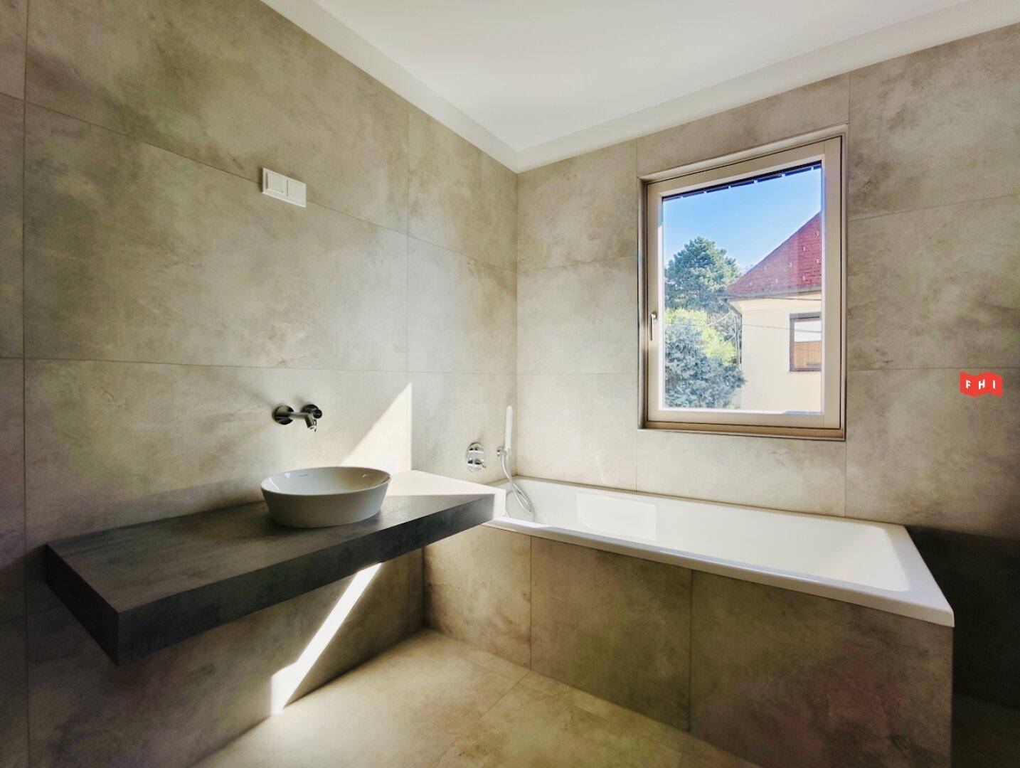 Helles Badezimmer mit Badewanne, Einzelwaschbecken und Fenster, das Tageslicht hereinlässt.