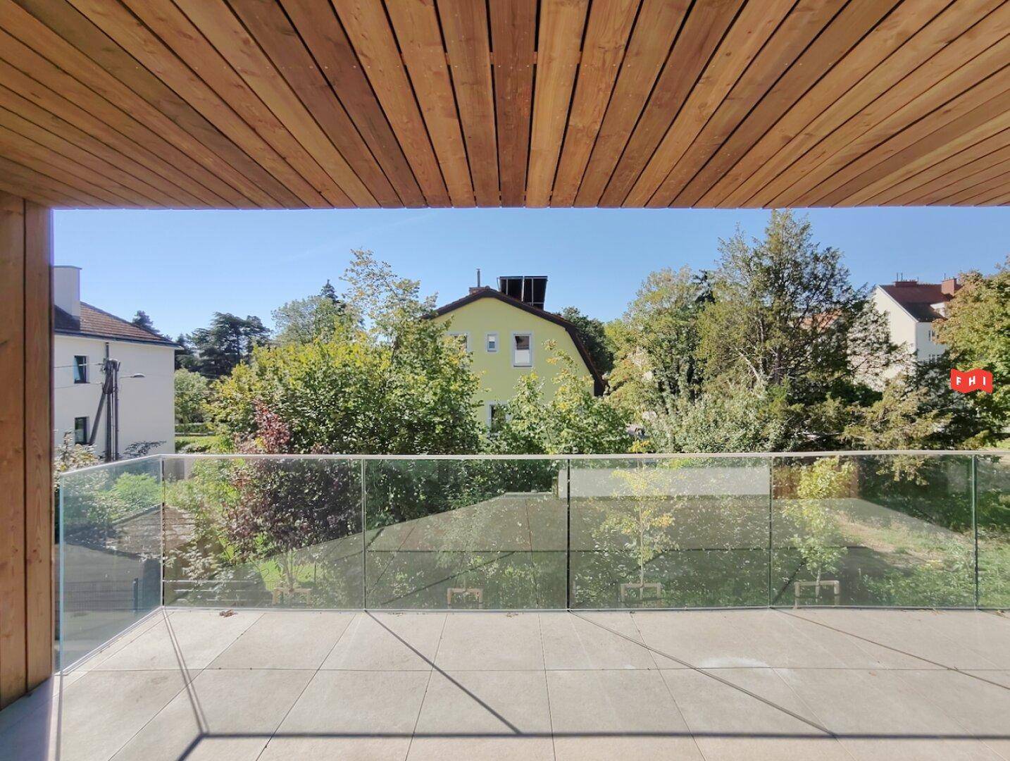 Balkon mit Glasgeländer und Holzdecke, bietet einen weiten Blick auf die grüne Umgebung.
