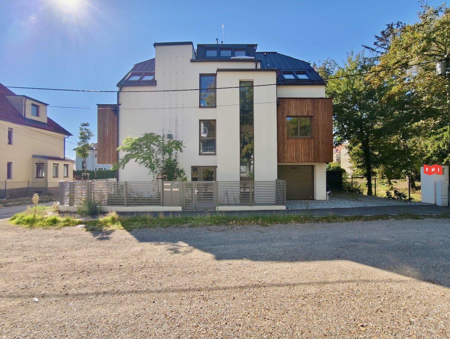 Ansicht der modernen Wohnanlage mit weißer Fassade, Holzdetails und sonnigem Außenbereich.