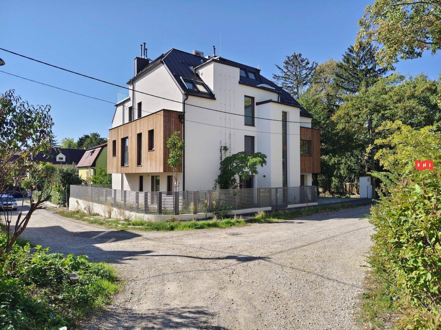 Seitenansicht des modernen Gebäudes mit weißer Fassade, Holzverkleidung und umlaufendem Zaun.