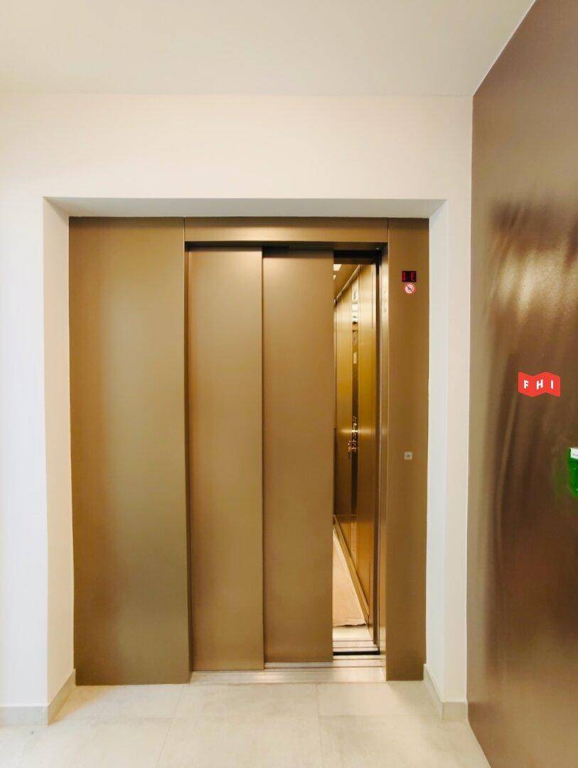 Moderner Aufzug mit braunen Schiebetüren in einem gepflegten Treppenhaus des Gebäudes.