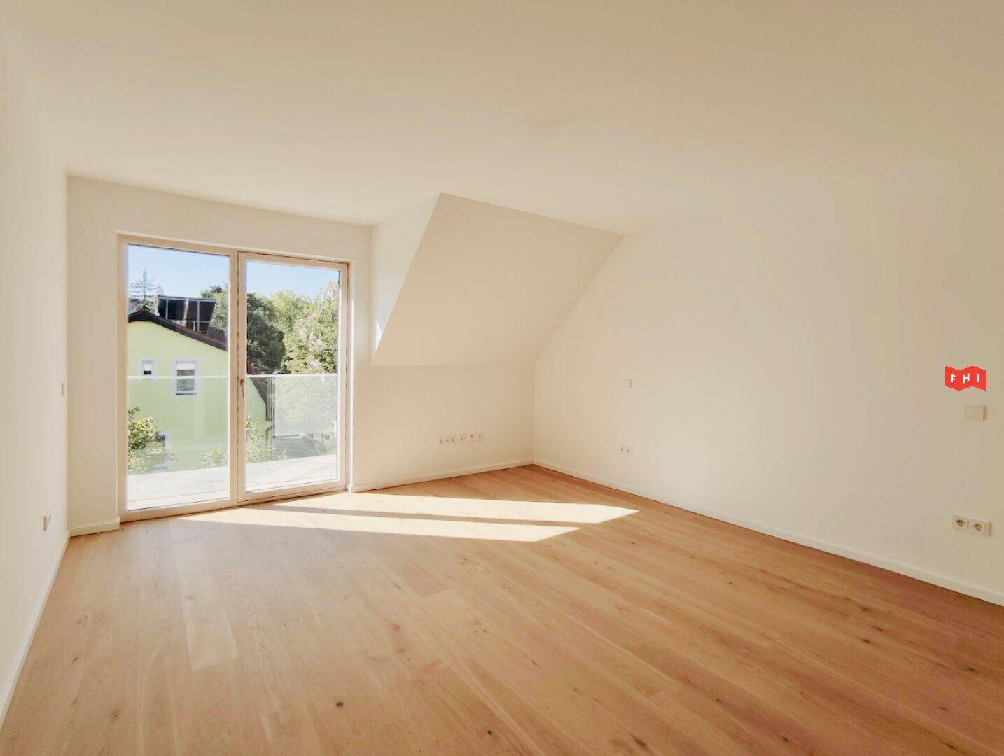 Lichtdurchflutetes Zimmer mit Holzboden, Dachschräge und Zugang zu einem Balkon.