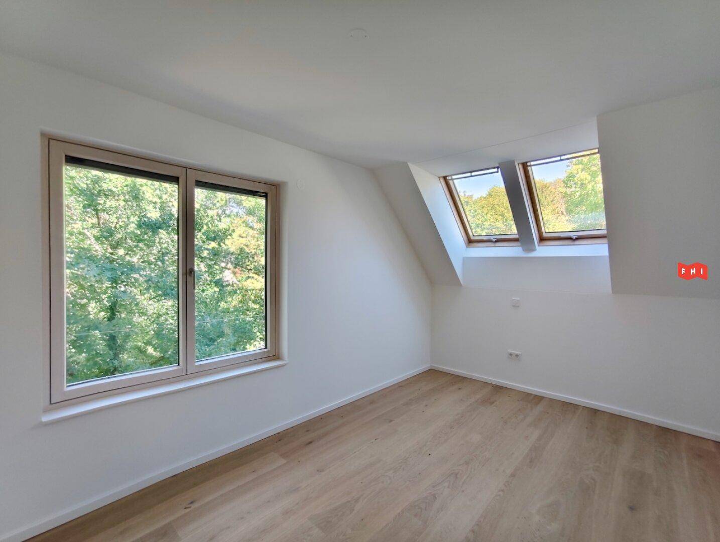 Helles Zimmer im Dachgeschoss mit Holzboden, großen Fenstern und Blick ins Grüne.