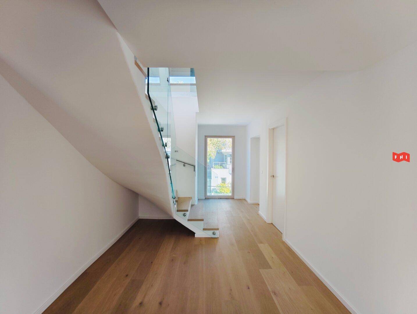 Heller Flur mit moderner Holztreppe, Glasgeländer und Zugang zu weiteren Räumen.