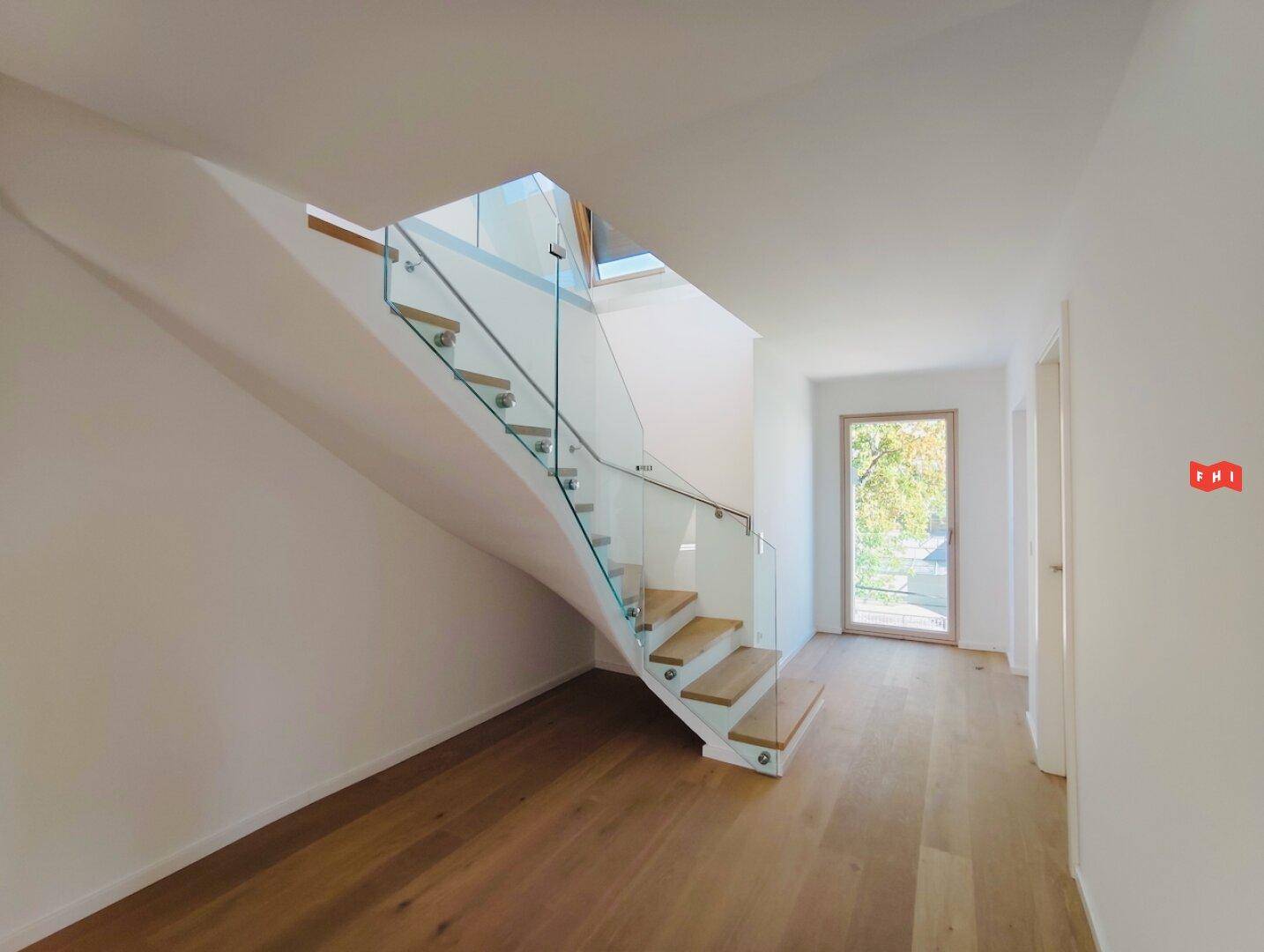 Heller Flur mit moderner Holztreppe, Glasgeländer und Zugang zu weiteren Räumen.