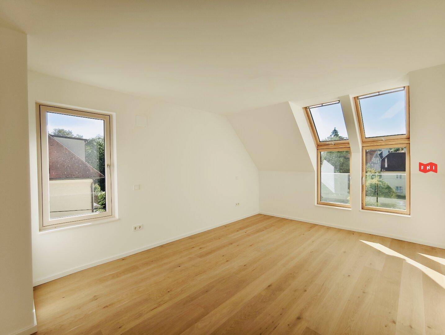 Helles Zimmer im Dachgeschoss mit Holzboden, großen Fenstern und Blick ins Grüne.