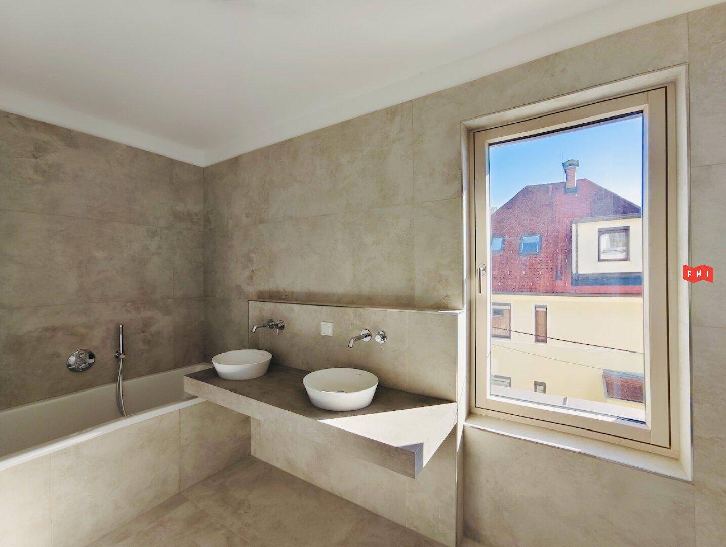 Modernes Badezimmer mit Badewanne, zwei Waschbecken und Fenster mit Stadtblick.