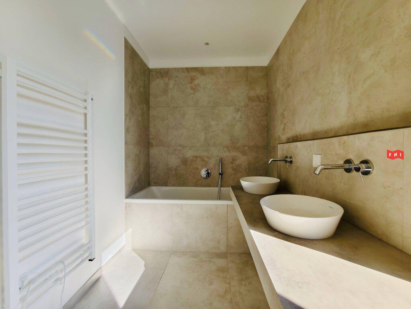 Elegantes Badezimmer mit Badewanne, zwei Aufsatzwaschbecken und beheiztem Handtuchhalter.