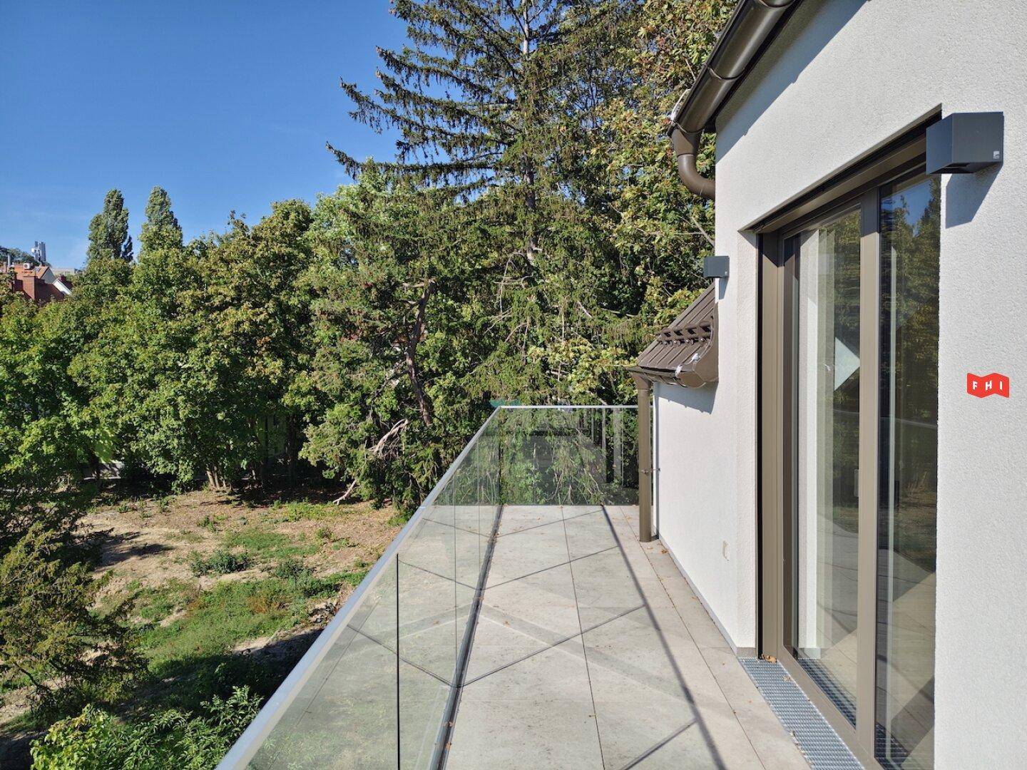 Langer Balkon mit Glasgeländer und weitem Blick auf die umliegende grüne Landschaft.