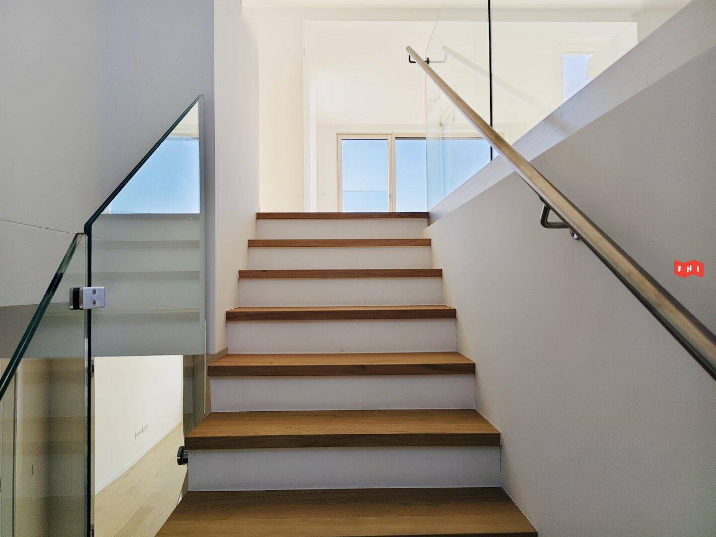 Moderne Holztreppe mit Glasgeländer, die in ein helles Obergeschoss führt.
