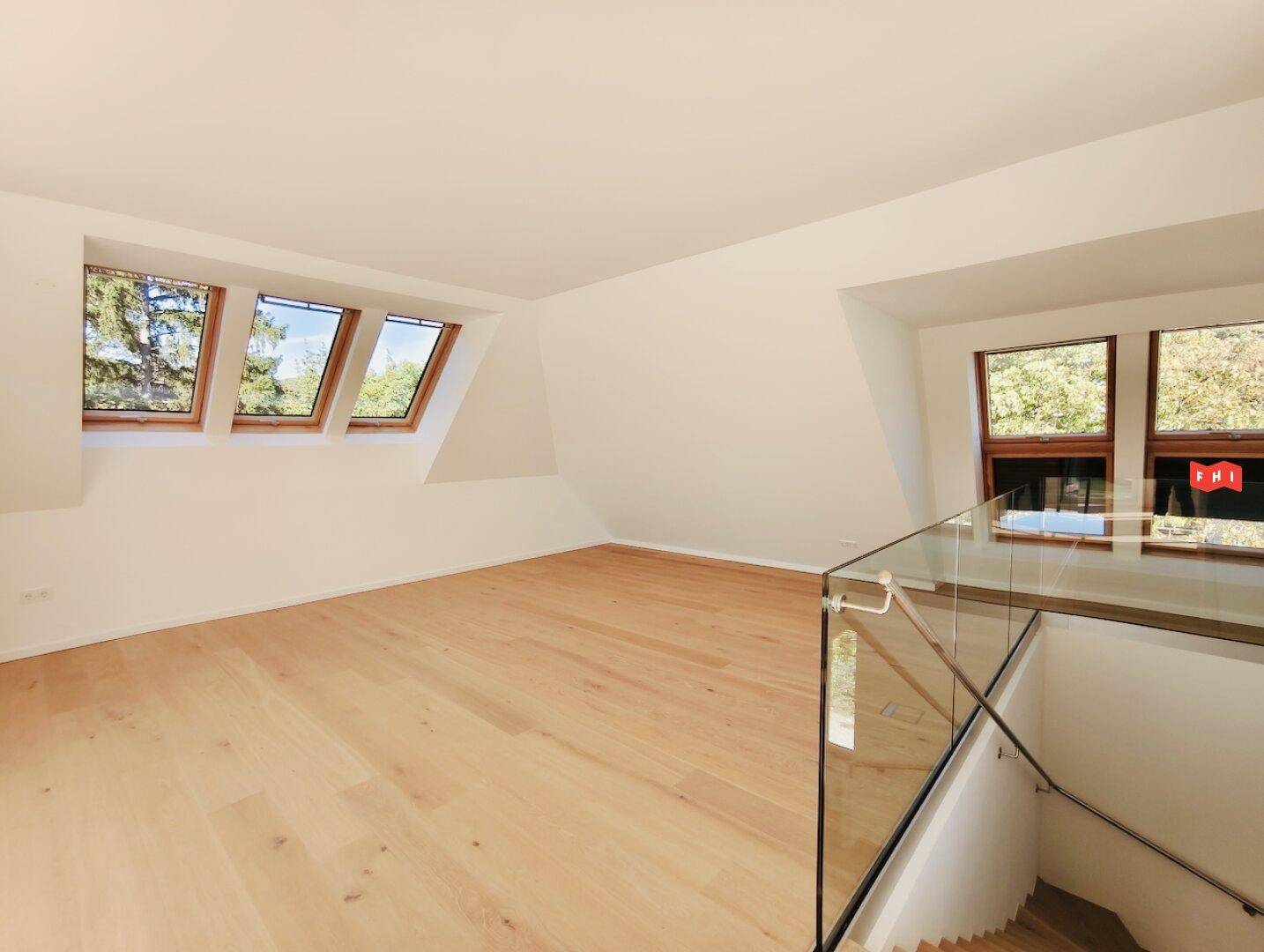 Helles Zimmer im Dachgeschoss mit Holzboden, Dachfenstern und Blick ins Grüne.