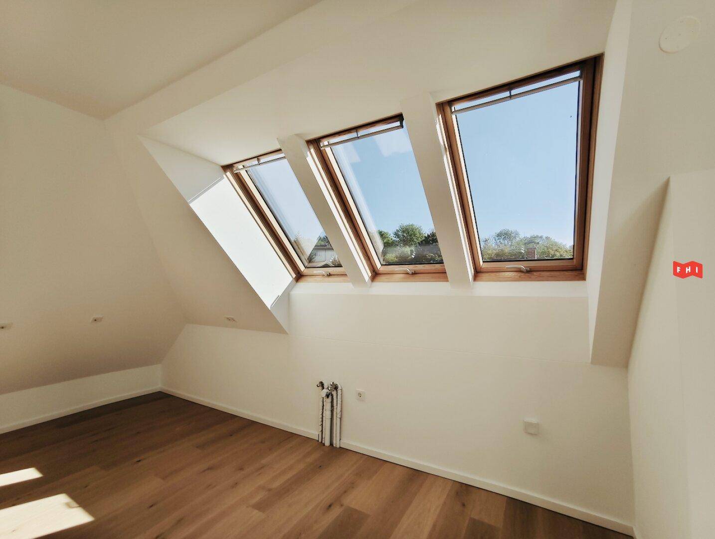 Helles Zimmer im Dachgeschoss mit Holzboden, Dachfenstern und viel Tageslicht.