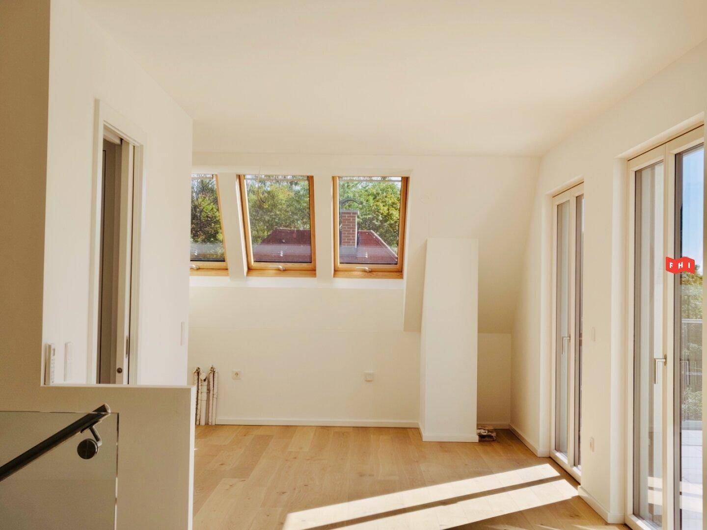 Helles Zimmer im Dachgeschoss mit Holzboden, Dachfenstern und Balkonzugang.