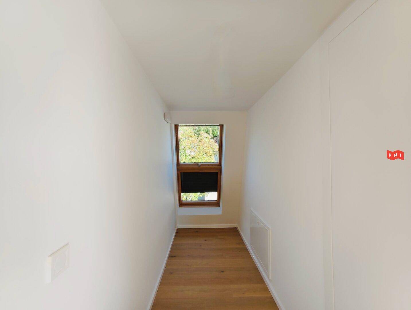 Heller Flur mit Holzfußboden und Fenster, das Tageslicht hereinlässt und eine grüne Aussicht bietet.