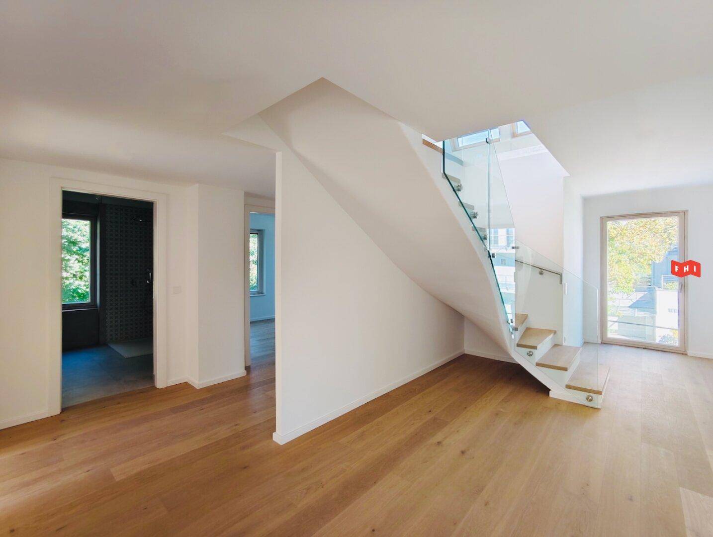 Heller Eingangsbereich mit Holztreppe, Glasgeländer und Zugang zu weiteren Wohnräumen.