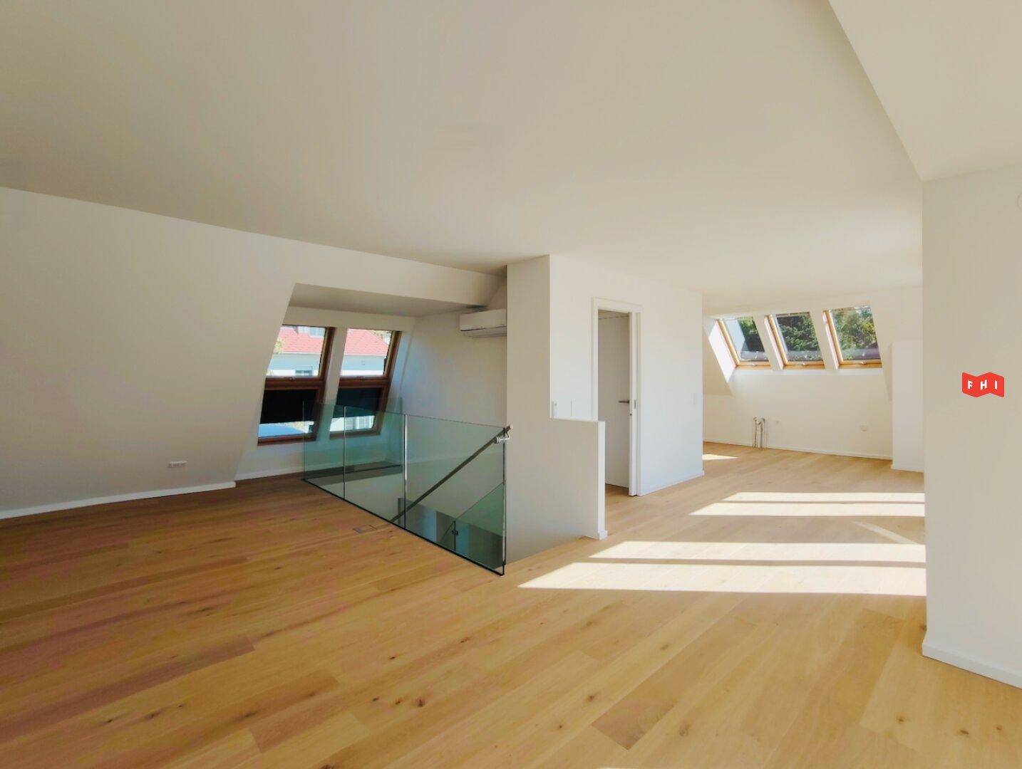 Offener Wohnbereich mit Holzboden, modernem Glasgeländer und vielen Dachfenstern für viel Licht.