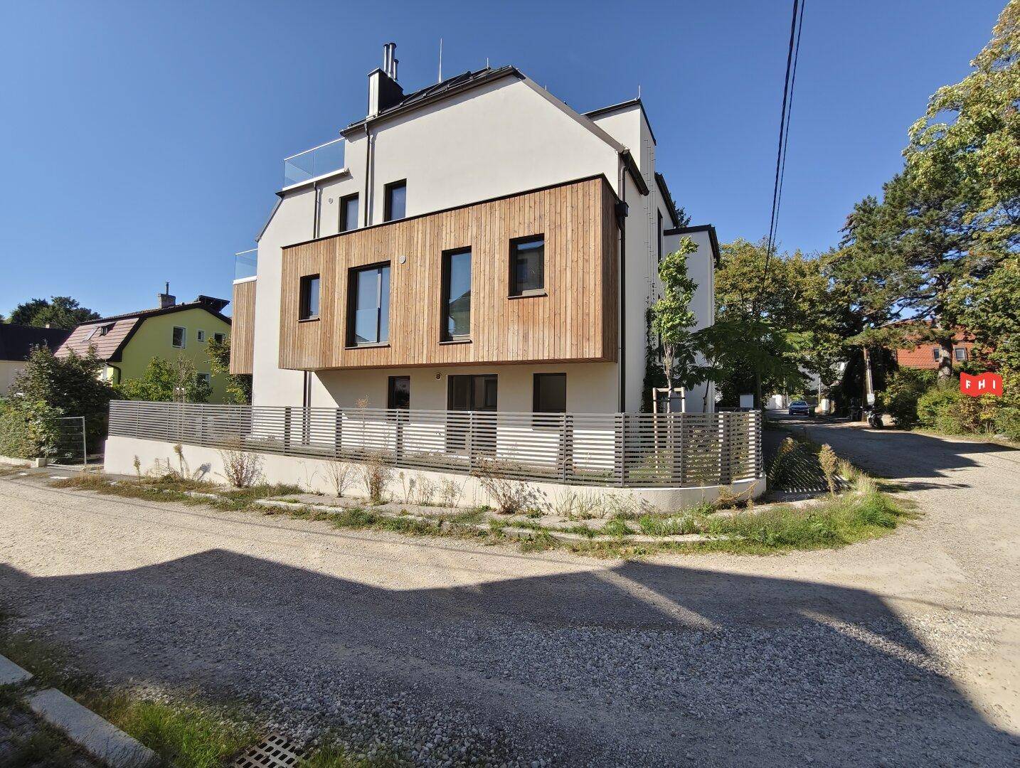 Zeitgenössisches Wohnhaus mit weißer Putzfassade, Holzverkleidung und Balkonen in sonniger Lage.
