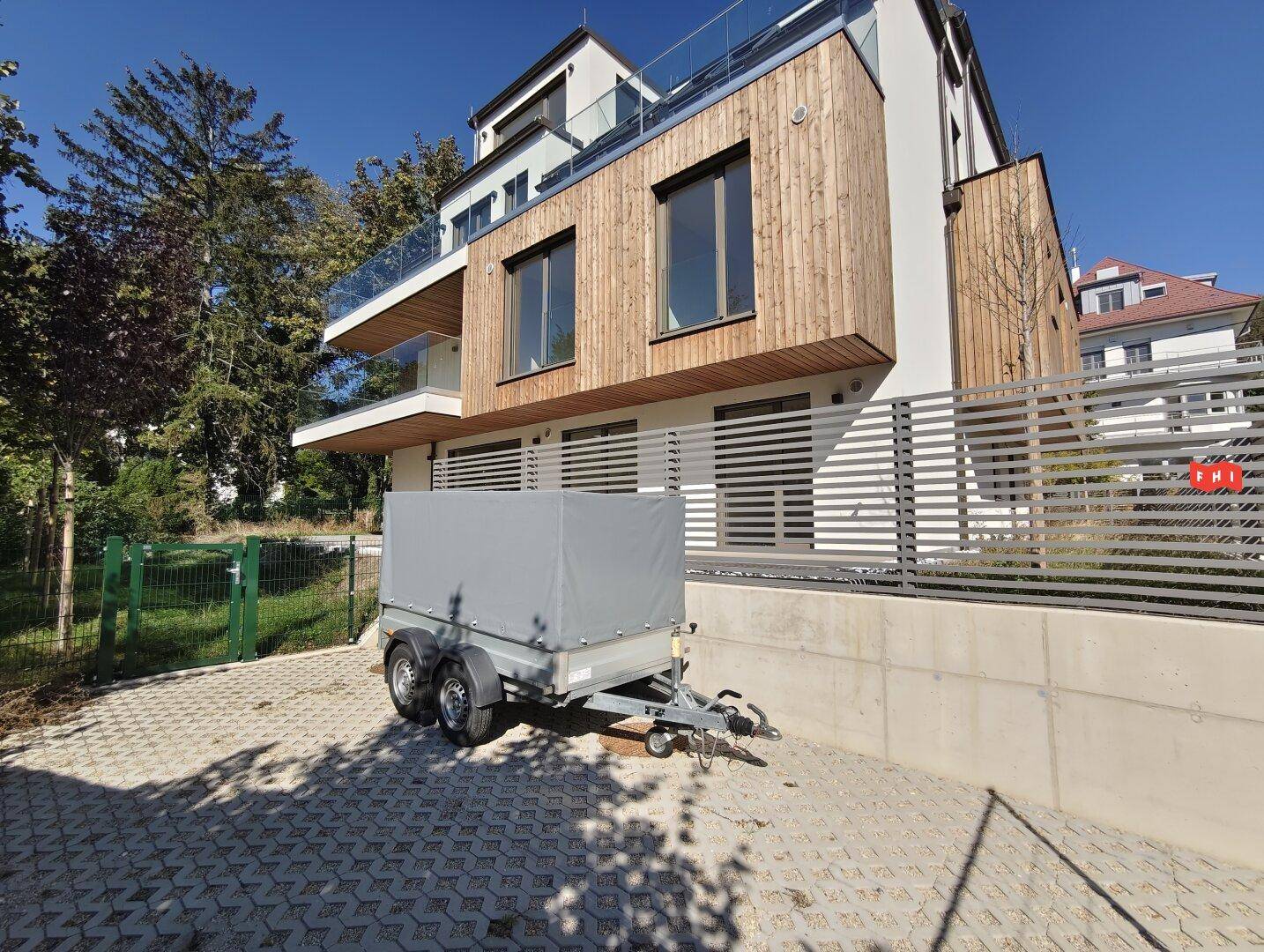 Modernes Wohnhaus mit Balkonen und Holzverkleidung, umgeben von Bäumen und Grünflächen.