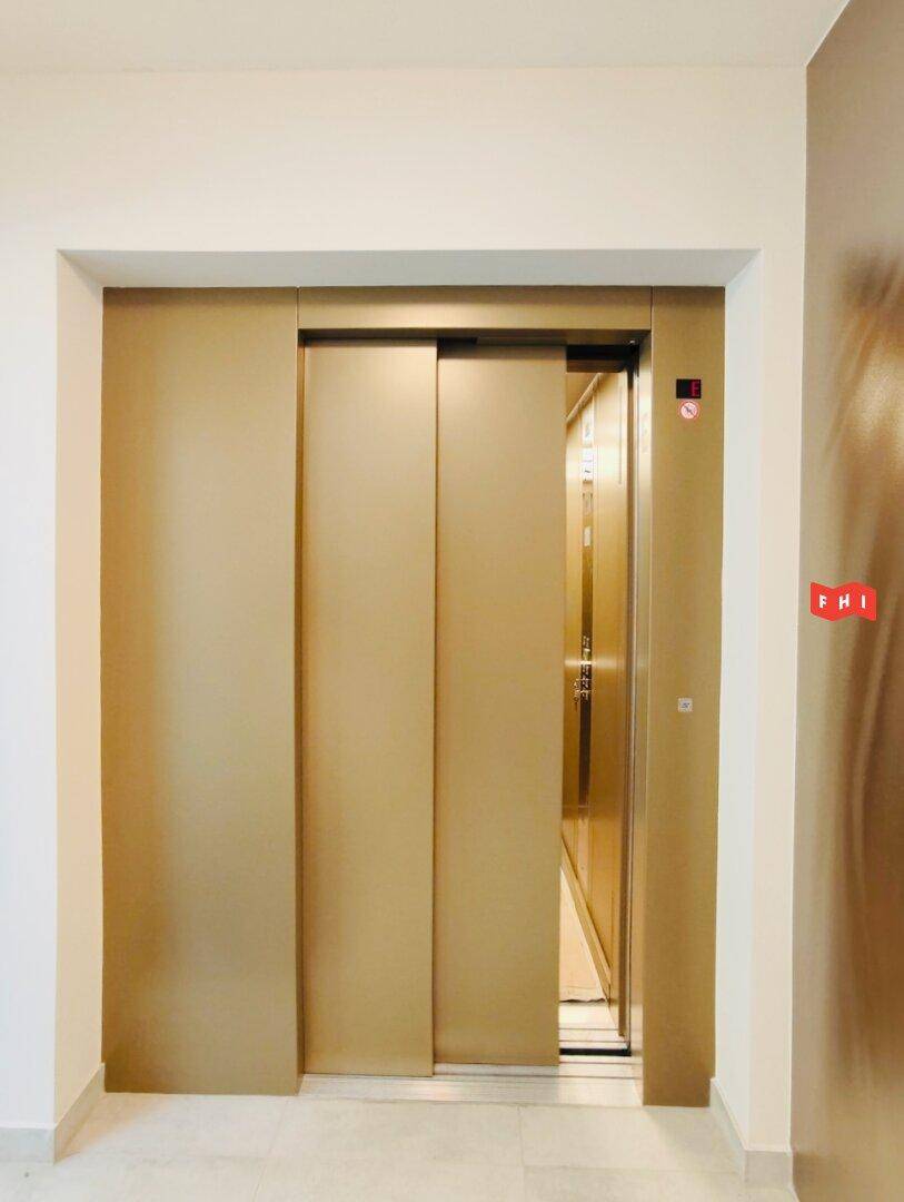 Moderner Aufzug mit goldenen Türen in einem hellen Flur, der barrierefreien Komfort bietet.