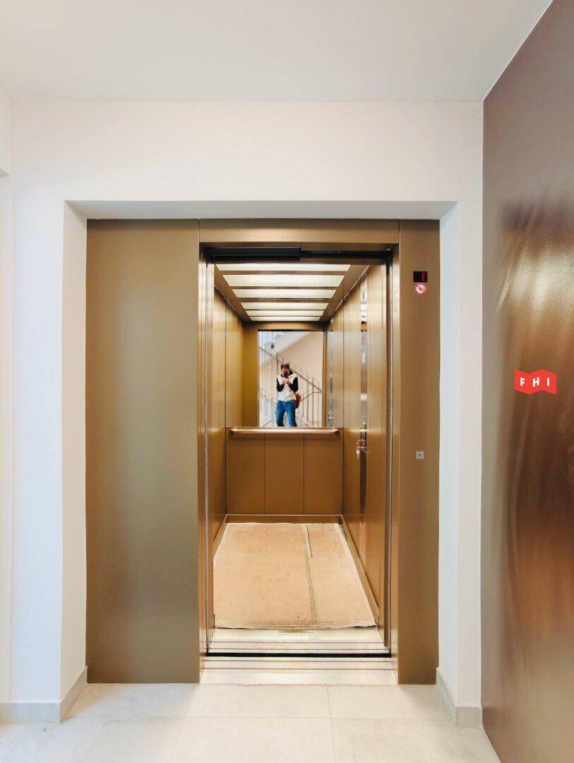 Geräumiger Aufzug mit Spiegelfläche und goldenen Wänden, der ein modernes Design aufweist.