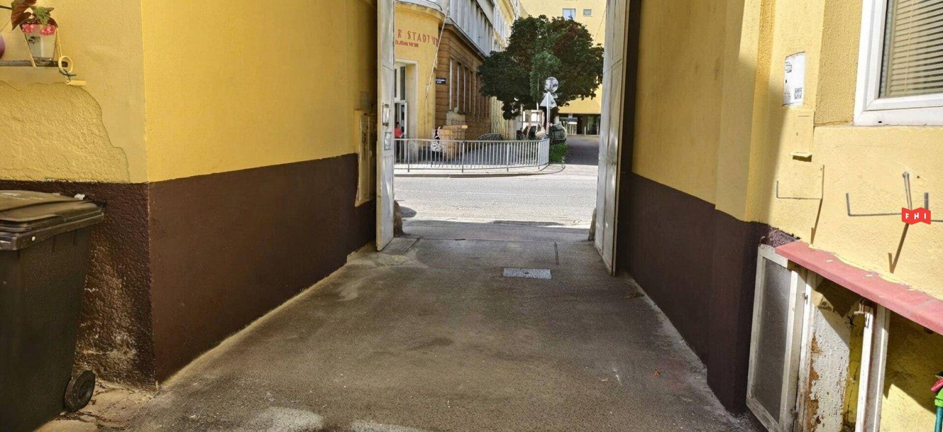 Durchgang vom Innenhof zur Straße, umgeben von gelben Wänden und einem Blick auf die Stadt.