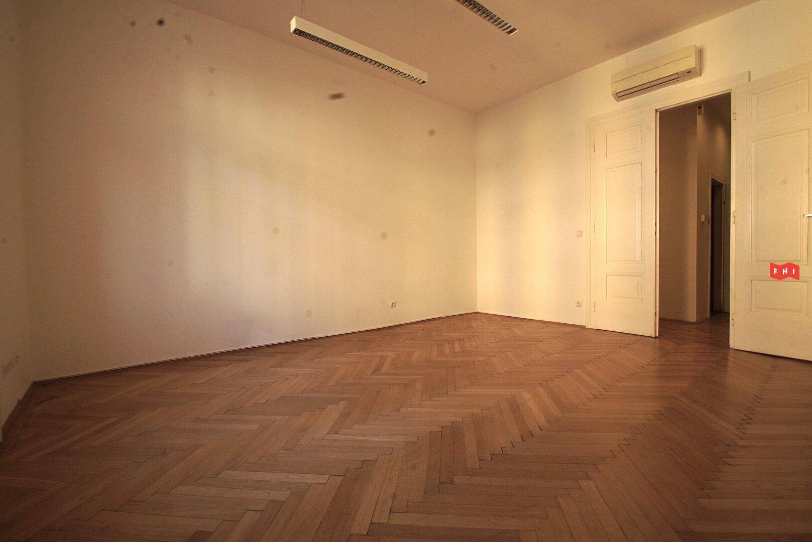 Heller Raum mit Fischgrätparkett, Deckenleuchten, Klimaanlage und Doppeltüren, ideal für Büro oder Wohnen.