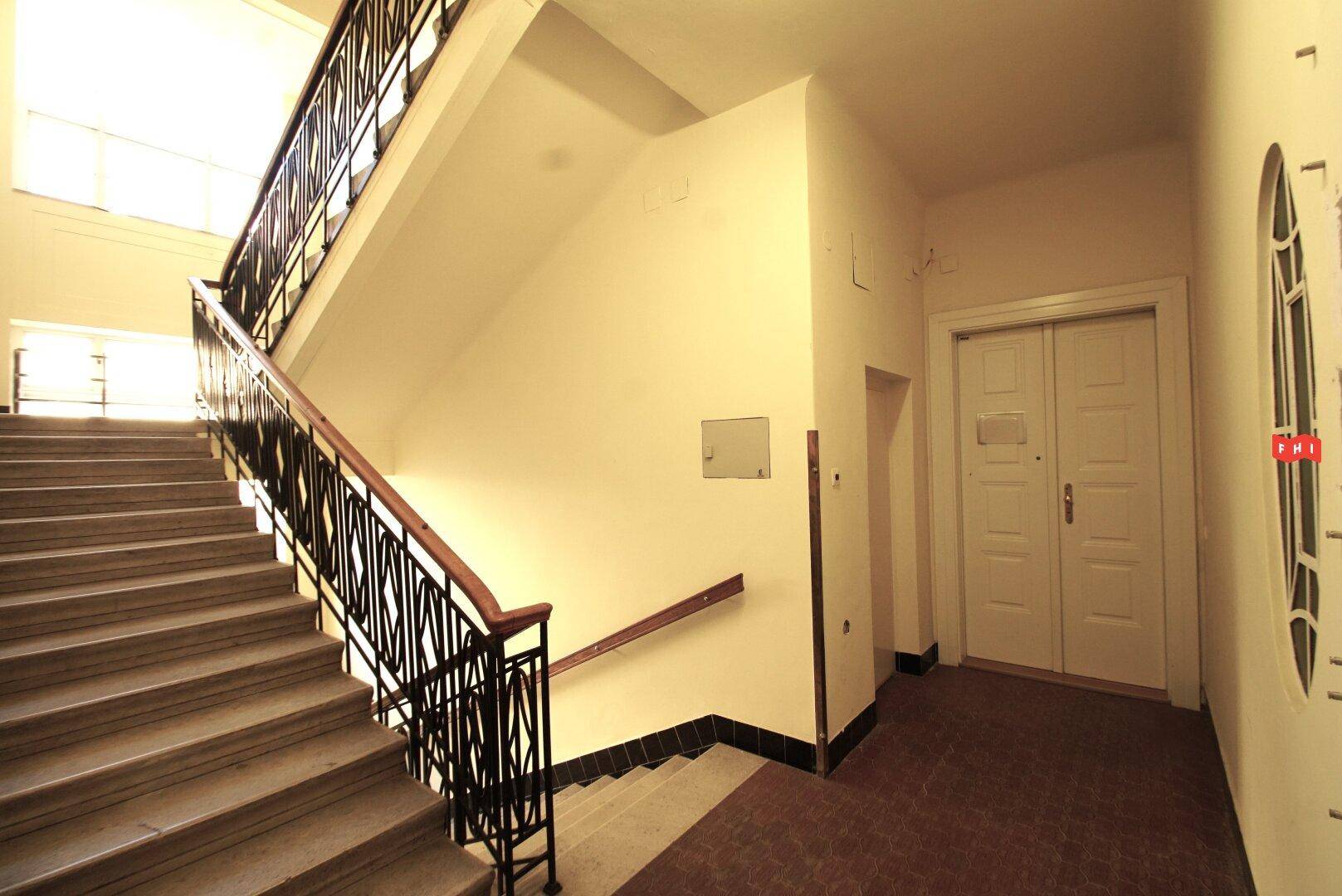 Geräumiges Treppenhaus mit Marmorstufen, schmiedeeisernem Geländer und hohen Decken in einem Altbau.