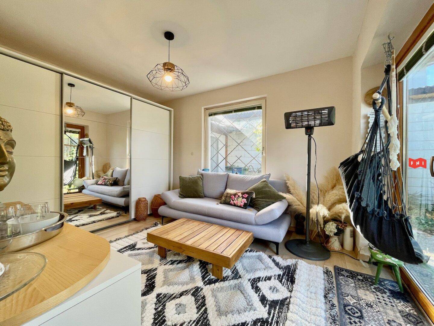 Helles Wohnzimmer mit modernem Teppich, beigem Sofa und Spiegelschränken, mit Blick in den Garten.