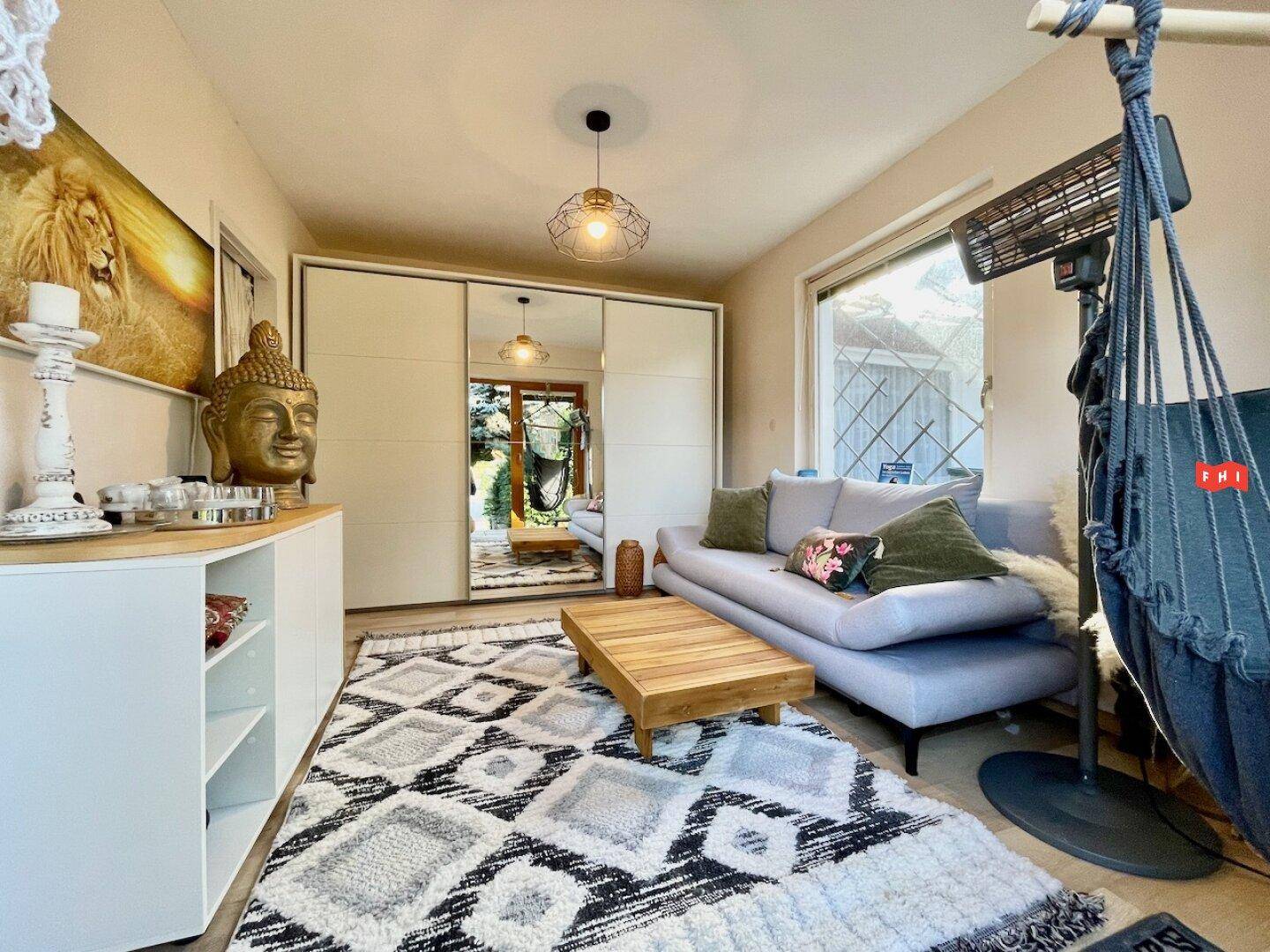 Gemütliches Wohnzimmer mit beigem Sofa, Holztisch und großem Teppich, hell durch Tageslicht.