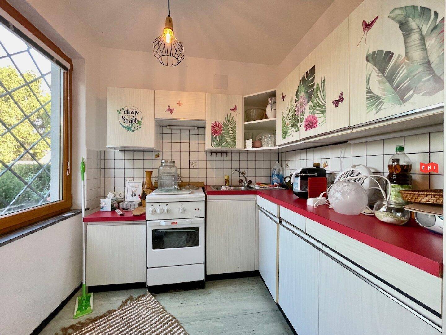 Einfache Küche mit weißen Schränken, roten Arbeitsplatten und Fenster mit Blick ins Grüne.