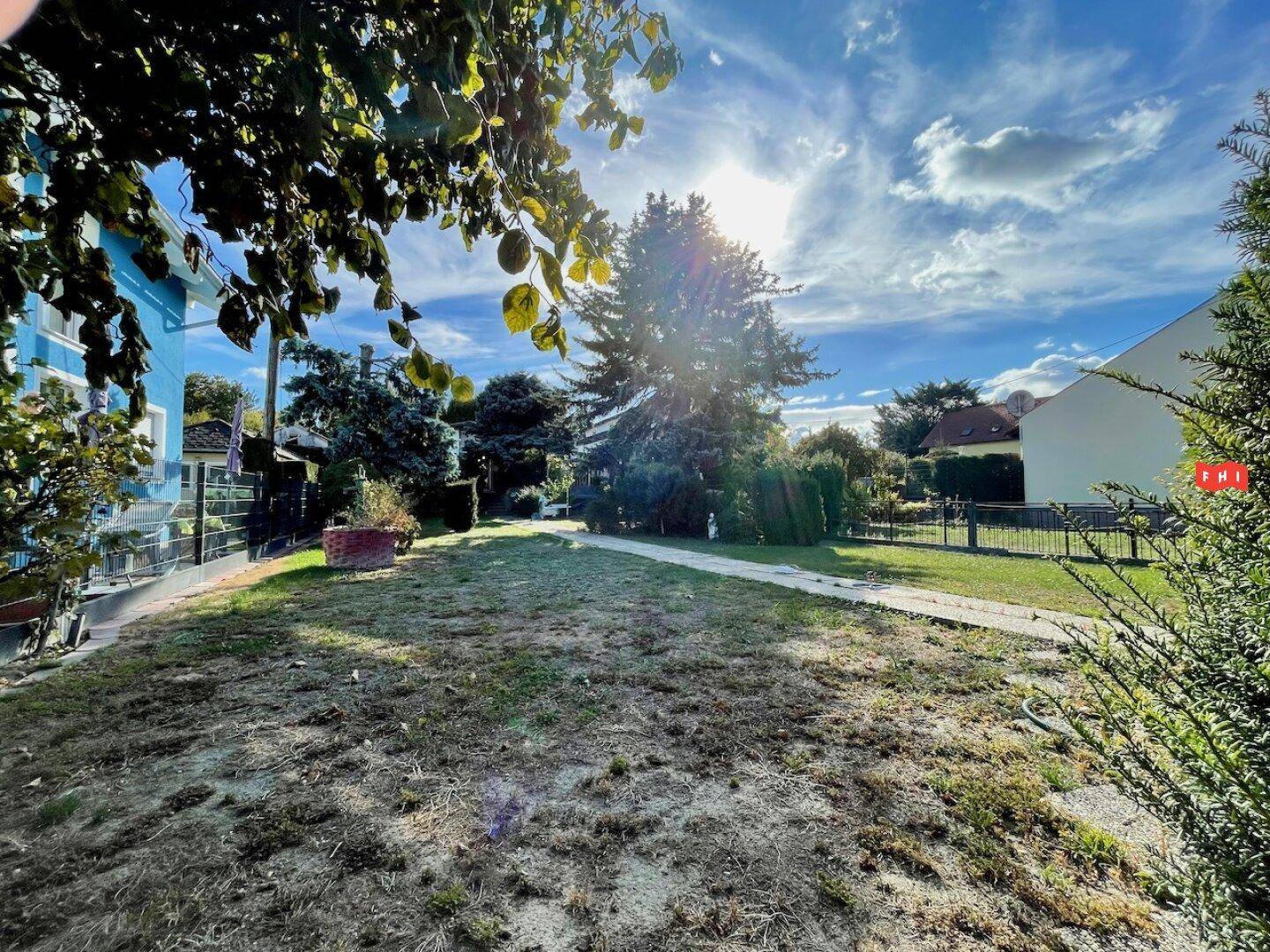 Weitläufiger Garten mit Rasenfläche und Bäumen, die das Grundstück umgeben, unter blauem Himmel.