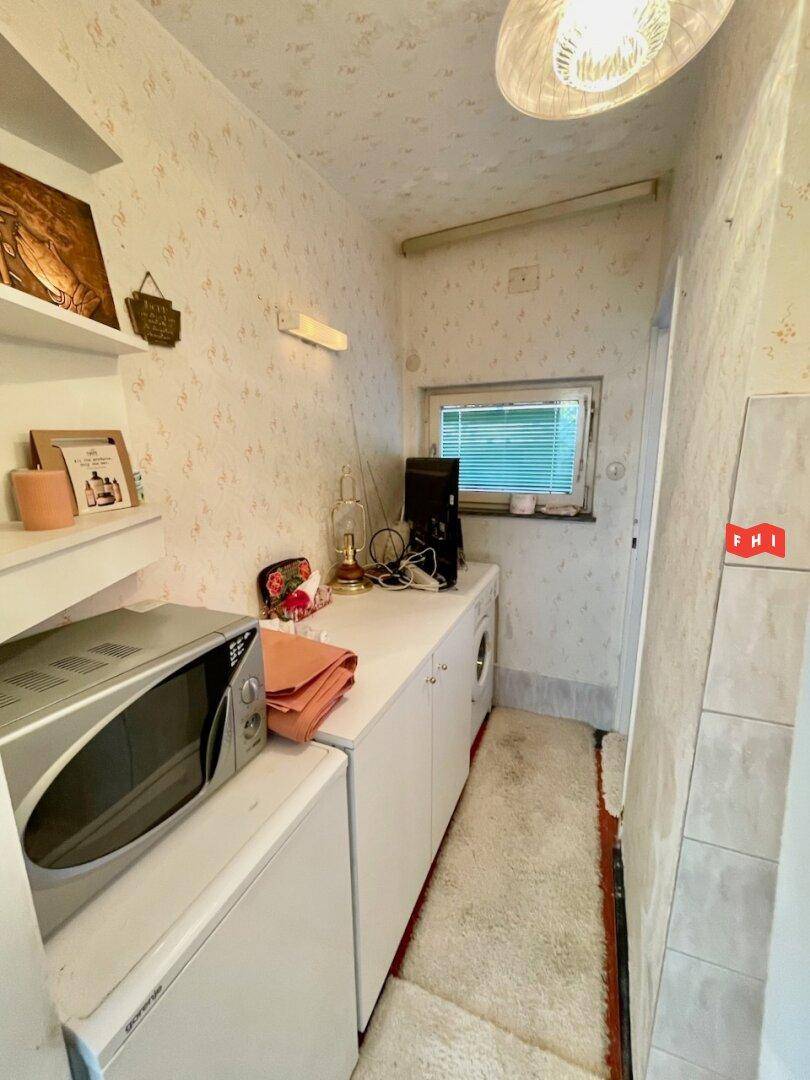 Kleiner Hauswirtschaftsraum mit Waschmaschine, Mikrowelle und Fenster, funktional eingerichtet.