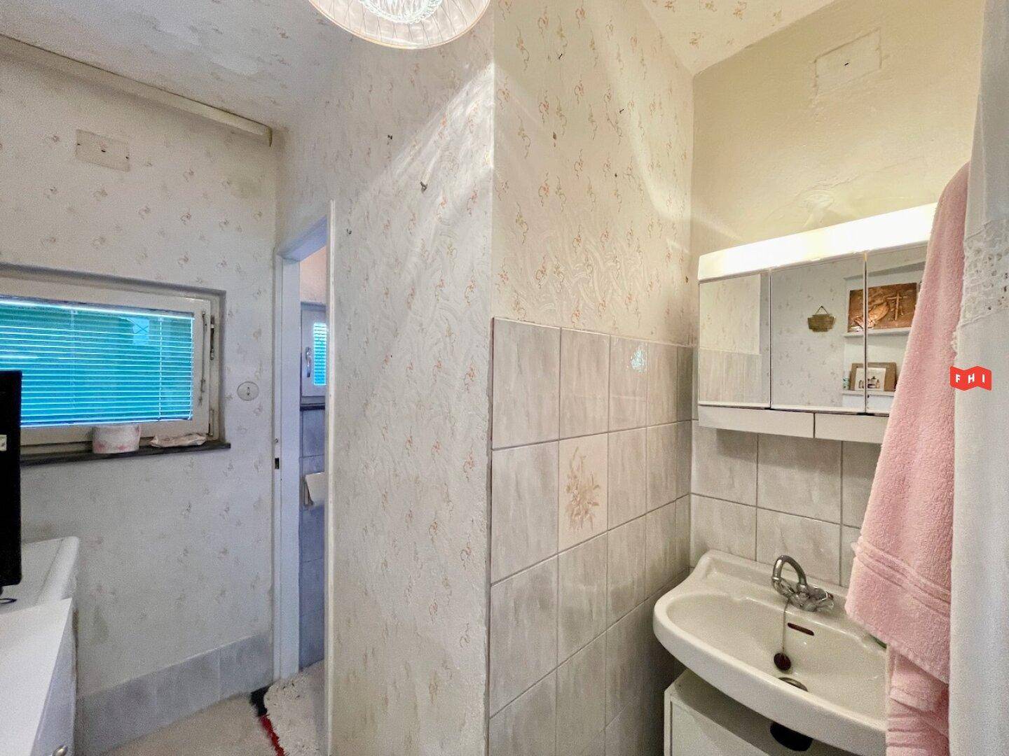 Schmaler Raum mit Waschbecken, Spiegelschrank und Fenster, dient als Hauswirtschaftsraum.