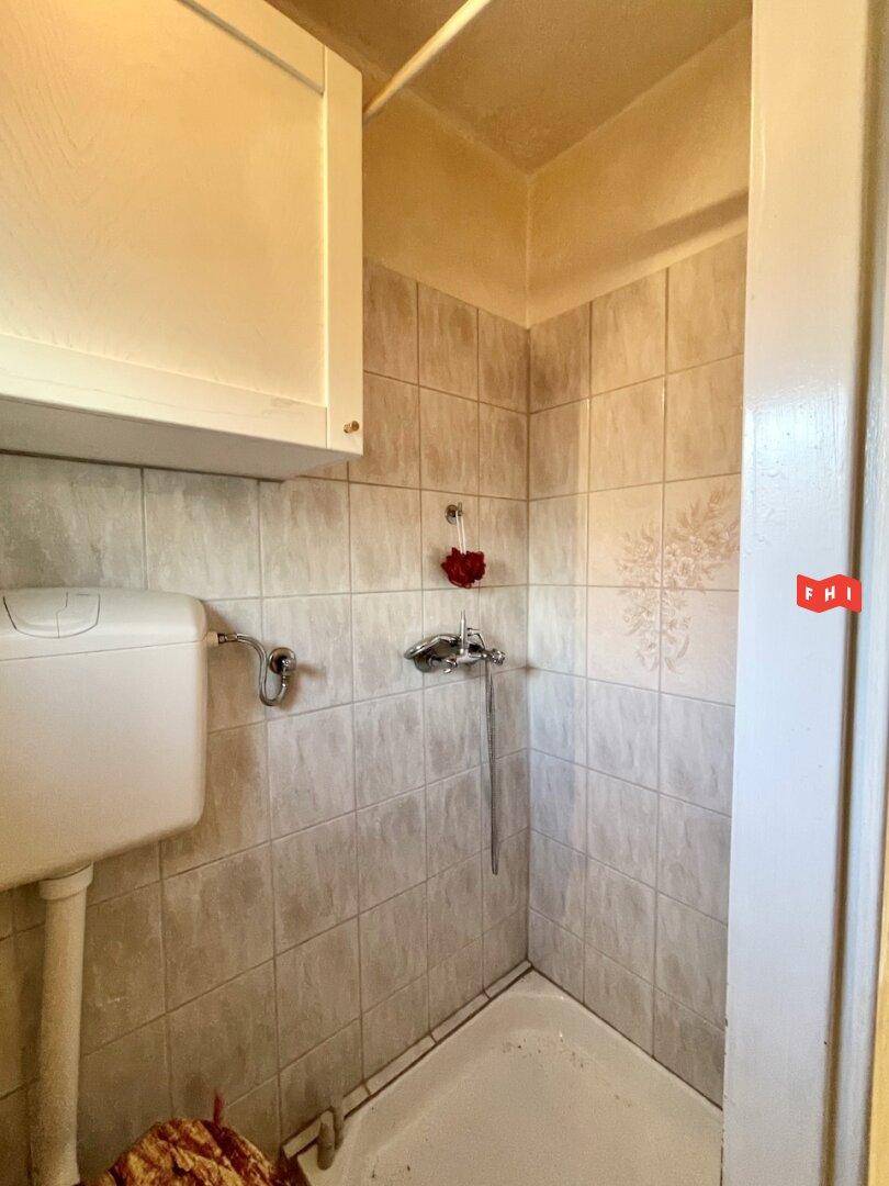 Einfache Duschkabine mit Fliesen an den Wänden und einem WC in einem kleinen Badezimmer.