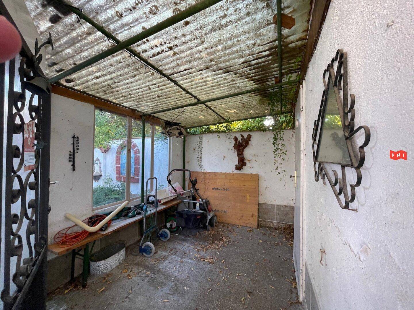 Überdachter Außenbereich mit Wellblechdach, genutzt als Abstellfläche für Gartengeräte und Möbel.