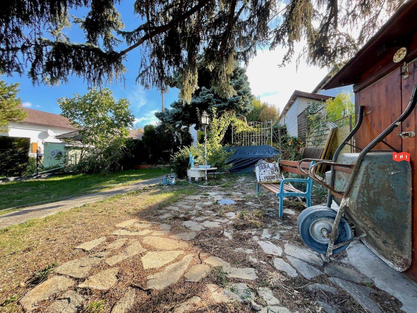 Rustikaler Gartenweg aus Steinplatten führt durch das grüne Grundstück mit Bäumen und Bänken.