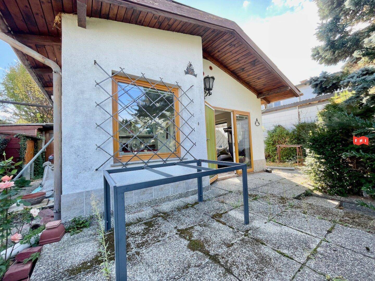 Gepflasterter Terrassenbereich neben dem Haus mit einem Metalltisch und Blick ins Grüne.