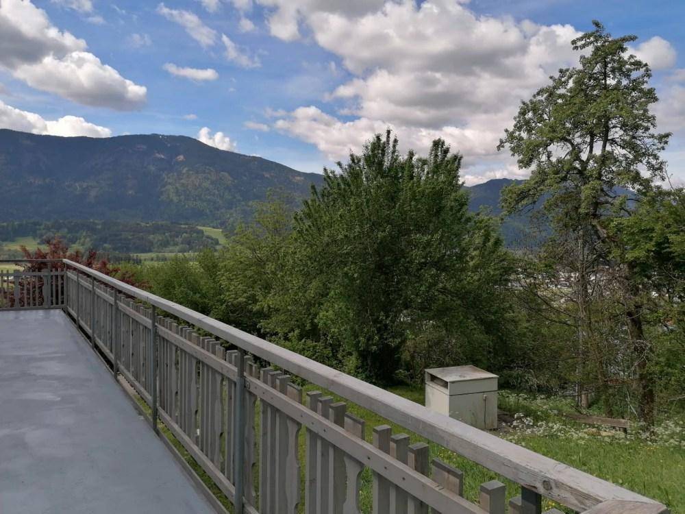 Weitläufiger Ausblick vom Balkon auf die grüne Berglandschaft unter bewölktem Himmel.