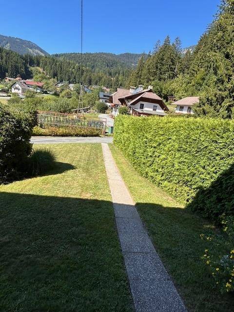 Blick auf einen Gartenweg mit Hecke und Häusern in der Ferne.