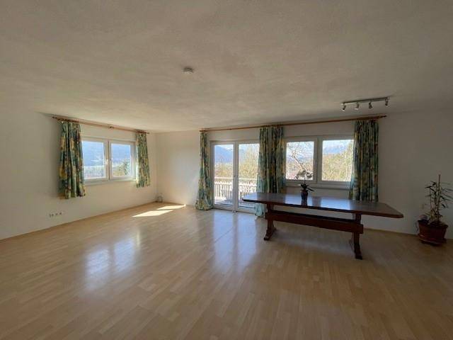 Geräumiges Wohnzimmer mit hellem Parkettboden, großen Fenstern und Balkonzugang.