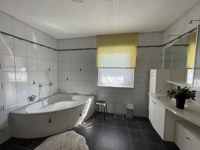 Helles Badezimmer mit weißen Wandfliesen, dunklem Boden und einer Eckbadewanne.