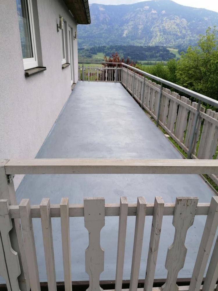 Langer, leerer Balkon mit Holzbalkongeländer und Panoramablick auf die grüne Landschaft.