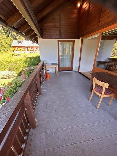 Überdachter Balkon mit Fliesenboden, Holzgeländer und Zugang zum Innenbereich.